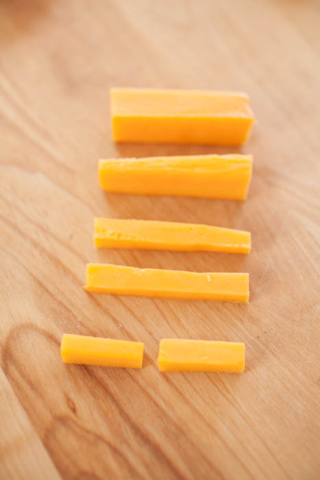 sticks of cheese in smaller and smaller sizes on a cutting board.