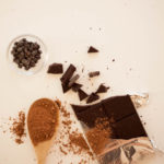 a spoon with cocoa, chocolate bar, and chocolate chips on a white background