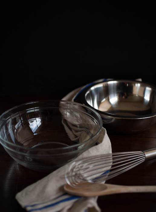 glass bowl, metal bowl, whisk, wooden spoon, and dishcloth