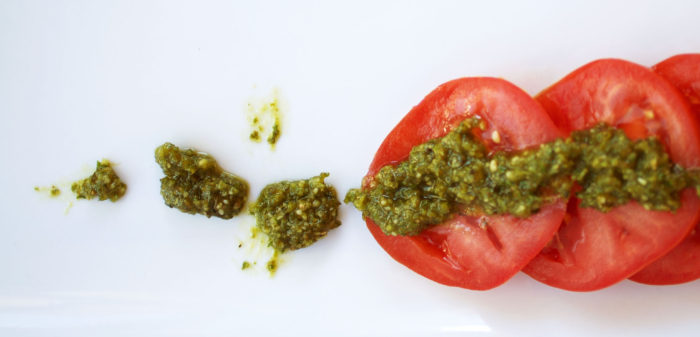 red tomato slices, green pesto on a white background