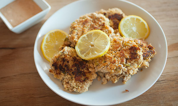 pan-fried salmon cakes on a plate with lemons and sauce 