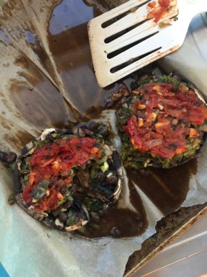 two mushrooms stuffed with veggies and black beans and topped with tomato sauce 