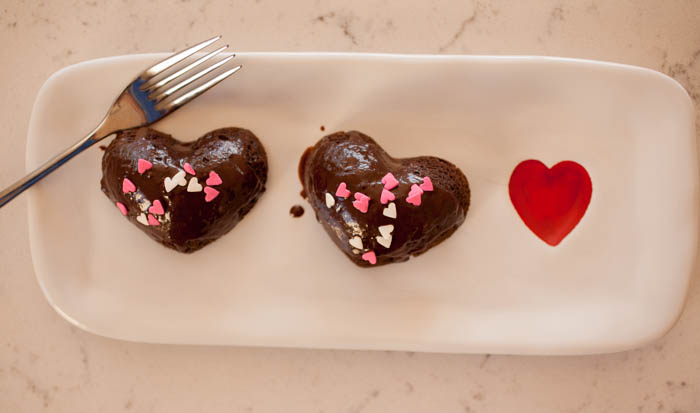 Two cakes glazed with ganache on a tray with a heart 