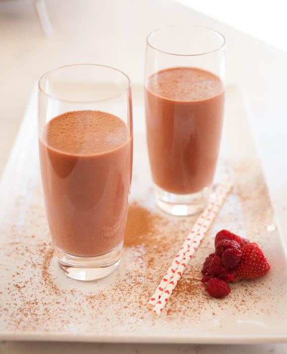 Two glasses of chocolate raspberry smoothie with heart straws, strawberries, and raspberries