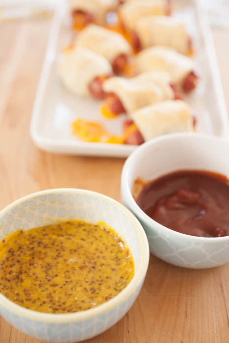 a mustard-based dipping sauce and ketchup-based dipping sauce in front of dough-wrapped crescent dogs
