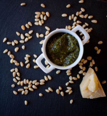 pesto in a white ramekin, pine nuts, and Parmesan cheese