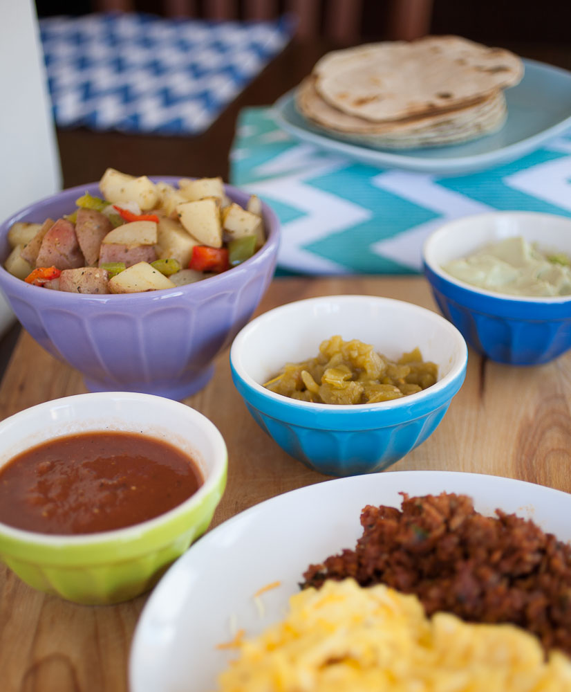 potatoes, green chile, salsa, avocado cream, and tortillas with chorizo and eggs in the foreground