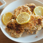pan-fried salmon cakes on a plate with lemons and sauce